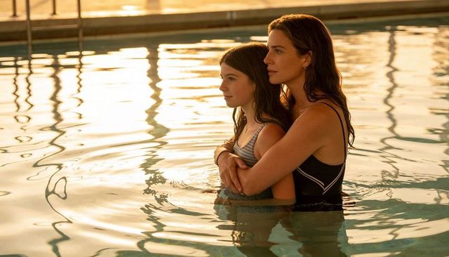 Mother embracing daughter in pool at golden hour, sunset swim and tender family bonding