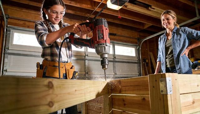 Young girl learning woodworking drilling power drill with safety goggles tool belt in garage