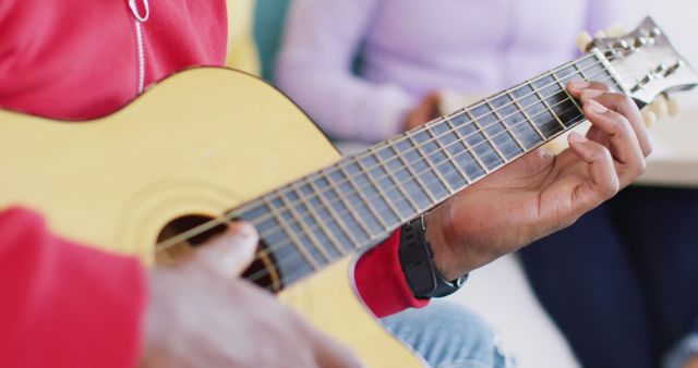 Midsection of african american man playing guitar with friends at home, in slow motion. Free time, friendship and lifestyle concept.