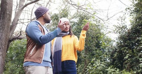 Couple exploring wooded trail pointing at trees during overcast autumn walk