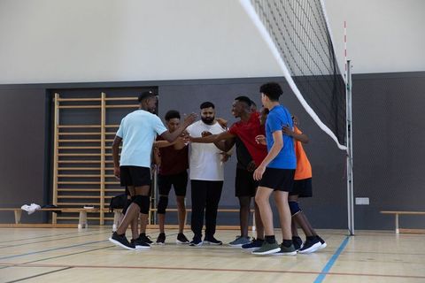 Multiethnic teen male volleyball team huddling with coach in indoor gym practice