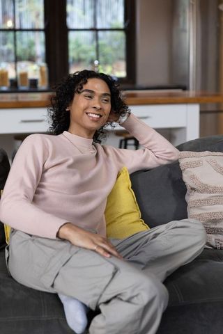 Relaxed non-binary person lounging on gray sofa with yellow cushion in cozy living room