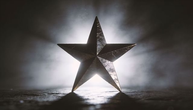 Backlit faceted metal star with halo and haze on textured surface, dramatic rimlight