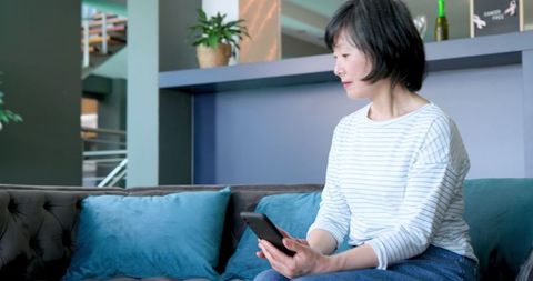 Senior Woman Using Smartphone on Sofa in Modern Living Room