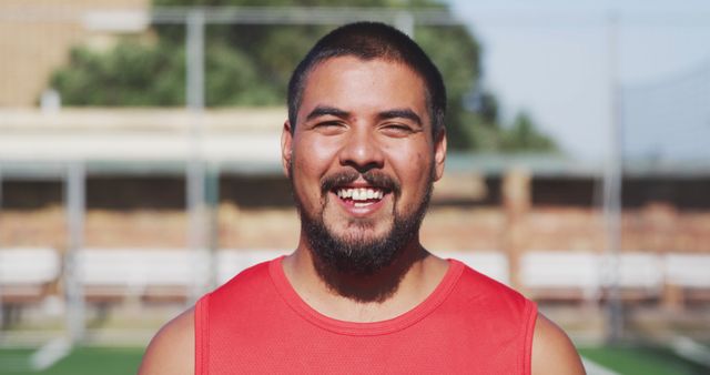 Portrait of biracial male football player looking at camera and smiling on outdoor pitch. Football and sports.