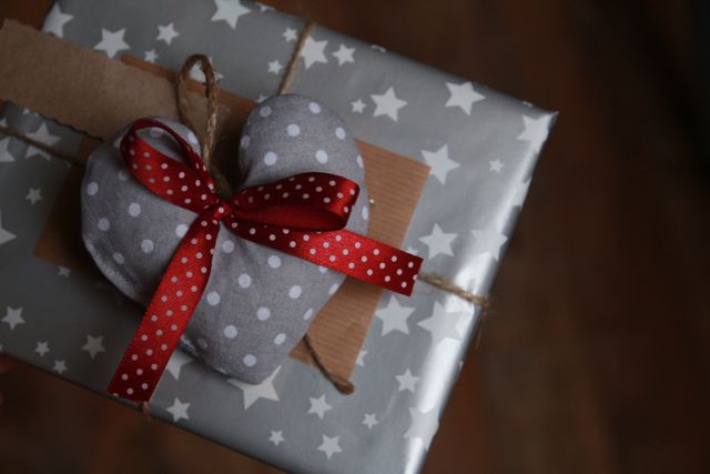 Heartwarming gift box wrapped with star-patterned paper, and decorated with a polka dot heart ornament and red ribbon. Ideal for holiday-themed content, special occasion marketing, and gift-giving ideas.