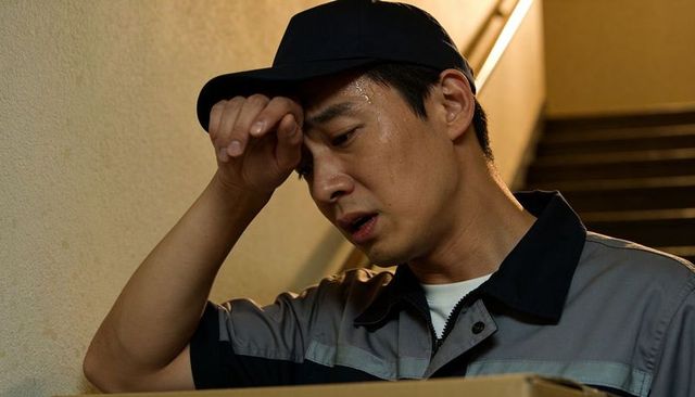Sweating courier wiping forehead while carrying box in narrow stairwell after shift