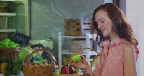 Smiling woman inspecting green apple at farmers market stall with wicker basket