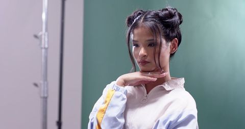 Asian model posing with hand under chin in studio portrait wearing pastel sports jacket