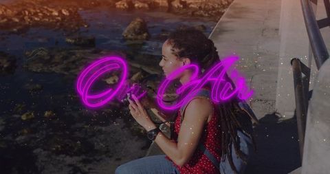 Sitting woman with backpack watching rocky coastline with neon on air overlay