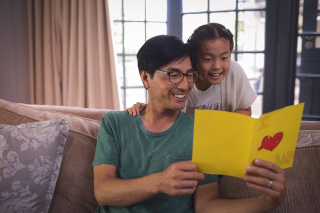 Father and daughter reading greeting card in living room at home