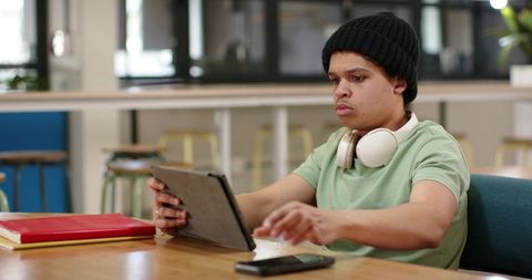 African american man working on tablet in coworking cafe with headphones and beanie