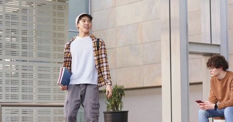 College students walking and sitting in urban campus plaza holding books and using phone