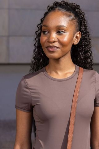 Smiling african woman standing by tiled wall wearing taupe top and crossbody strap