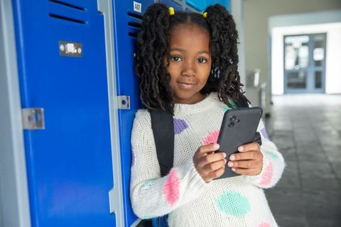 African american child holding smartphone in school hallways