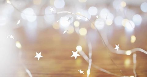 Glowing fairy lights creating warm bokeh on wood table with scattered star overlays