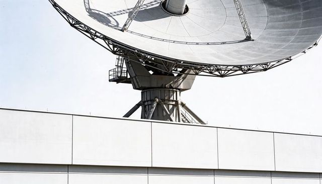 Parabolic satellite dish towering over rooftop parapet, industrial communication antenna