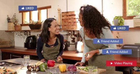Laughing women preparing vegetables on wooden island in rustic kitchen with social media badges
