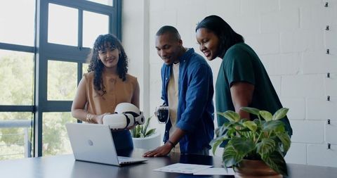 African american team collaborating with white robot and laptop in modern bright workspace