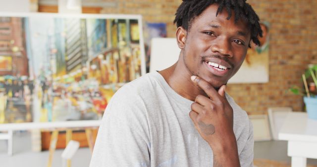 This image depicts a male artist smiling confidently in his studio, with an urban painting in the background. The setting conveys a sense of creativity and dedication to art, making it ideal for use in articles, blogs, and marketing materials related to creative professions, personal stories of artists, art schools, and artistic inspiration.