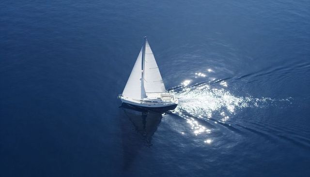 Sailboat gliding across deep blue ocean with sparkling wake and crisp white sails