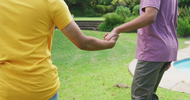 Midsection of biracial gay male couple holding hands walking in garden. staying at home in isolation during quarantine lockdown.