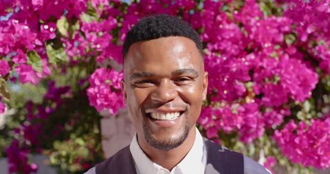 Joyful biracial man smiling by vibrant flowers