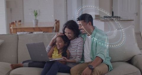 Family laughing on sofa around laptop sharing cozy online learning and streaming