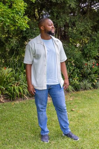 Man standing and looking up on backyard lawn wearing casual shirt, jeans and sneakers