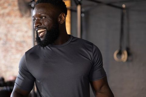 Laughing african american man posing in industrial gym wearing athletic shirt, muscular strength