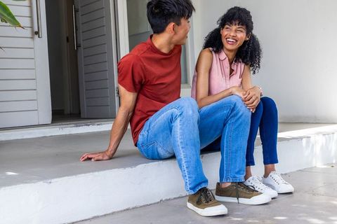 Young interracial couple laughing and chatting on front porch steps during sunny day