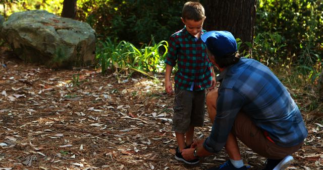 A young boy is having his shoe tied by an adult male in a natural outdoor setting, with copy space. This tender moment captures a caring interaction, between a parent and child, emphasizing the importance of guidance and support in a child's life.