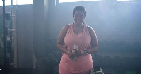 African american woman in pink activewear hydrating after workout in industrial gym