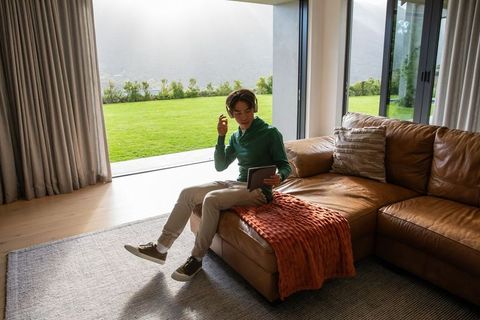 Asian man wearing headset and using tablet on leather chaise in modern living room