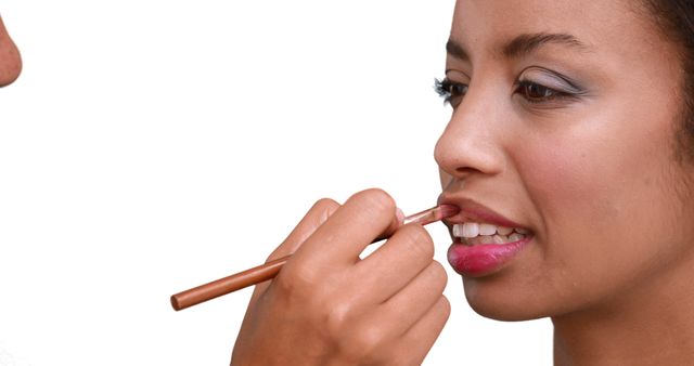 Make up artist putting lip gloss on models face on white background