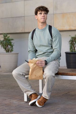 Contemplative college student sitting on campus bench eating lunch from paper bag