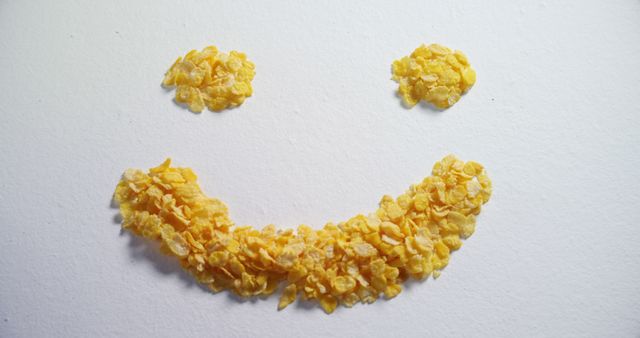Cornflakes are arranged in a smiley face pattern on a white background, with copy space. The playful arrangement of the cereal creates a cheerful and creative presentation.