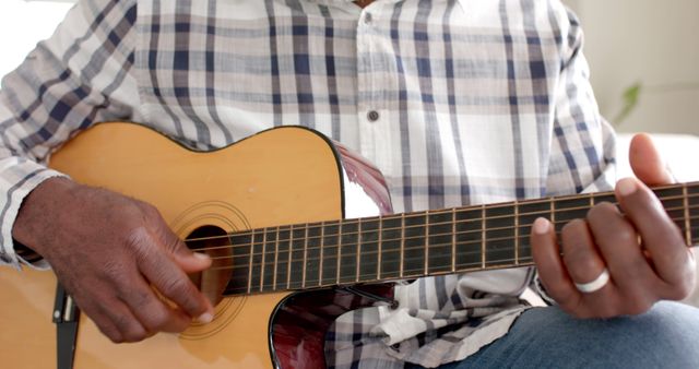 Close-up of individual playing acoustic guitar, showcasing finger placement and strumming technique. Appealing for music-related websites, educational material, or lifestyle blogs focusing on hobbies and relaxation.