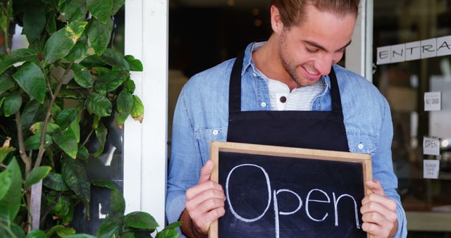 Portrait of smiling waiter showing chalkboard with open sign at cafe door 4k