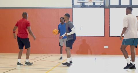 Five men playing basketball in indoor gym dribbling and defending during pickup game