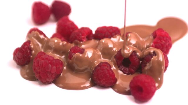 Rich chocolate sauce is pouring over fresh raspberries, creating an indulgent and delicious combination. Perfect for use in dessert recipes, food blogs, menus, and advertisements focusing on delicious sweet treats.