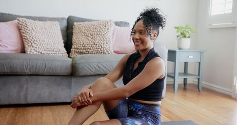 African american woman smiling on yoga mat in bright living room for home fitness
