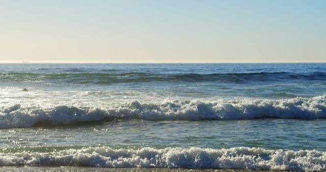 Photo captures early morning waves crashing on the beach, with the horizon visible under the clear sky. Ideal for travel websites, nature blogs, and backgrounds promoting relaxation and serenity.