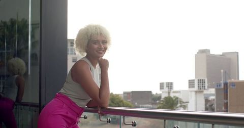 Confident woman in pink pants enjoying urban balcony view