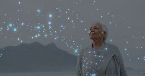 Senior woman gazing at shoreline amid dreamlike blue light particles