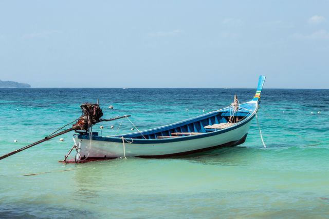 Traditional wooden longtail boat anchored in clear turquoise water, idyllic for travel and tourism content. Ideal for promoting tropical destinations, adventure travel agencies, or illustrating serene natural environments. Perfect for brochures, social media campaigns, and websites focusing on coastal and marine experiences.