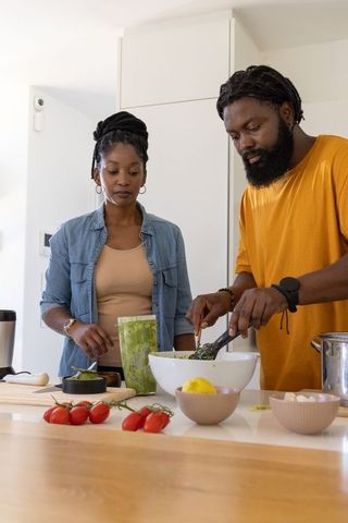 Couple preparing green pesto for meal prep on modern kitchen island
