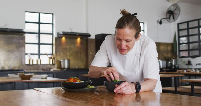Female chef garnishing plates with fresh ingredients in a stylish, modern kitchen. Perfect for content related to cooking techniques, culinary arts, professional chefs, recipe development, or kitchen aesthetics.