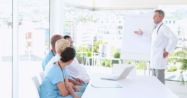 Doctor presenting training session to a team of healthcare professionals in a modern office with large windows and a whiteboard. This professional setting can be used to depict modern medical training, professional development, teamwork and leadership in a healthcare environment.