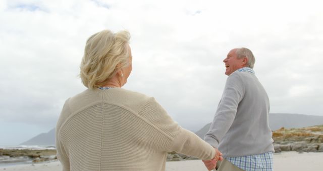 Happy senior caucasian couple holding hands and walking on beach. Retirement, summer, leisure, vacation and senior lifestyle, unaltered.